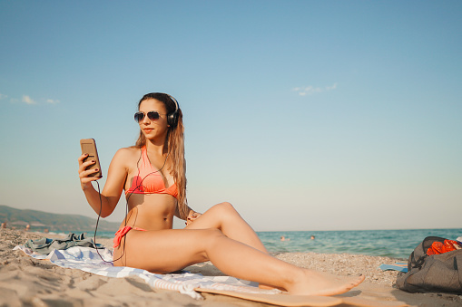Woman in pink bikini relaxing on the sandy beach and listening to music