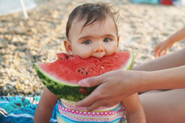 Mother feeding her little daughter with watermelon on a beach Mother feeding her little daughter with watermelon on a beach family beach vacations travel stock pictures, royalty-free photos & images