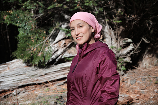 Woman with cancer wears pink scarf and jacket while walking in the woods