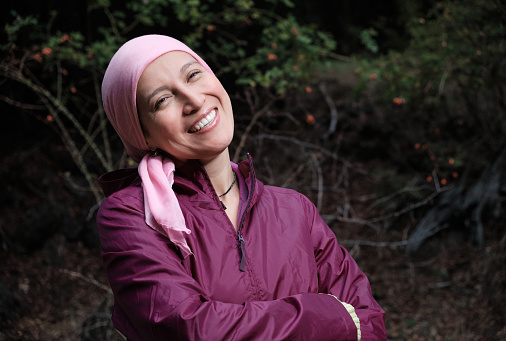 A woman with cancer wearing a headscarf smiles and looks at the camera showing hope and the will to live.