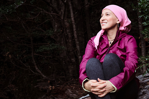 Medical and health concept.Young breast cancer survivor holding her knees while relaxing in the middle of nature.