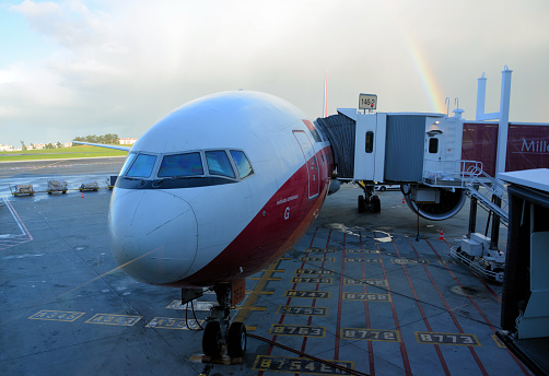 Lisbon, Portugal: TAAG Angola Airlines Boeing 777-300ER - front view of the aircraft at a jet bridge, rainbow in the background, aircraft model markings on the pavement for correct parking - Lisbon Airport aka Humberto Delgado Airport - TAAG Linhas Aéreas de Angola Airlines - D2-TEG Boeing 777-3M2(ER), named 'Sagrada Esperança', after 'Grupo Desportivo Sagrada Esperança', a football (soccer) club from Dundo, Lunda Norte province, founded and sponsored by diamond company Diamang (now Endiama).