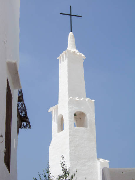 construcción típica española de una torre de iglesia blanca con una cruz católica construida según la arquitectura de las cícladas en menorca. en la torre hay una campana de la iglesia. cielo azul claro en el fondo - cycladic architecture fotografías e imágenes de stock