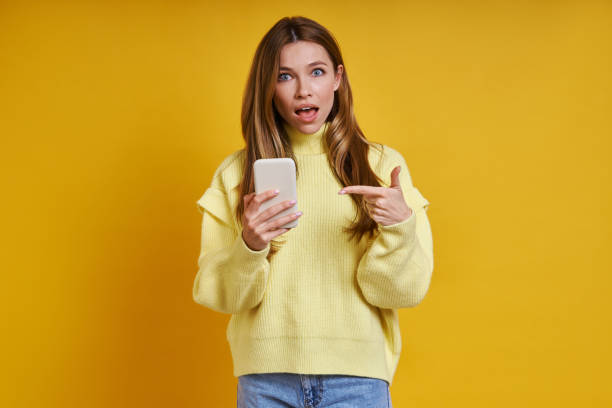 istock Surprised young woman pointing her smart phone 1400144547
