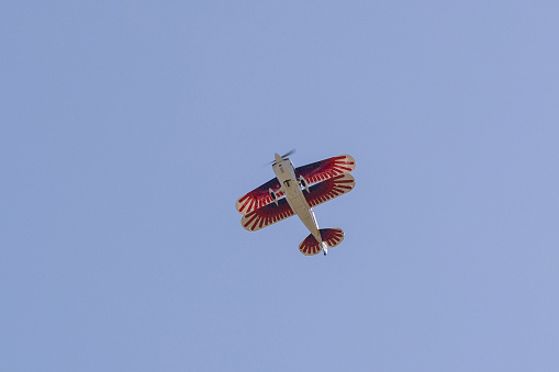 double wing stunt plane up in the sky. Looking at the underside of the wings. Bright red strips on wings