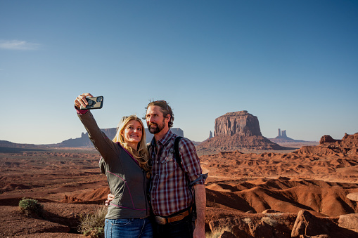 Young Couple Enjoying Bluffs and Cliffs in Monument Valley Tribal Park Taking a Selfie at dusk