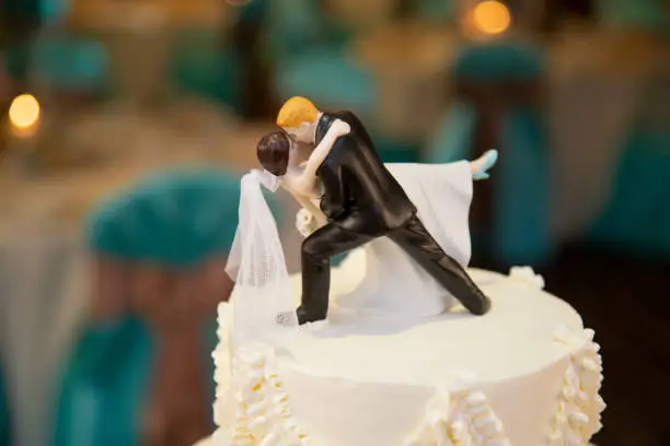 Caucasian bride and groom cake topper. Groom in black suit, bride in white wedding dress. Groom is dipping bride for the big kiss