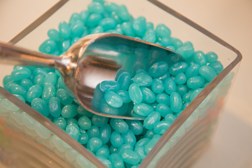 Turquoise jellybeans in square glass jar. Metal scooper dug into jellybeans