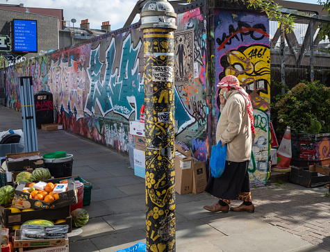 A man dressed in a middle eastern headscarf walks past a fruit stall at Brick Lane Market, held on Sundays in the East End of London, England, UK