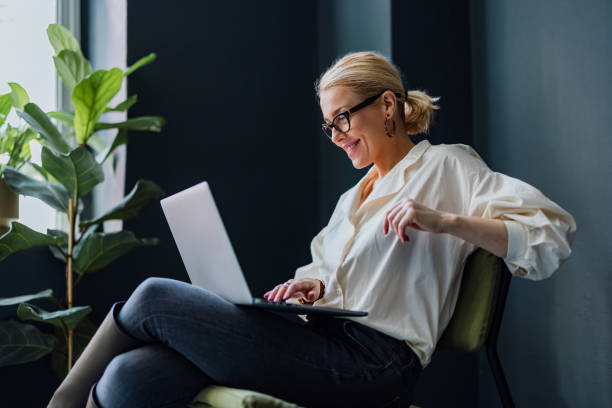 szczęśliwa kobieta biznesu korzystająca z laptopa w biurze - biała kobieta czyta w okularach zdjęcia i obrazy z banku zdjęć