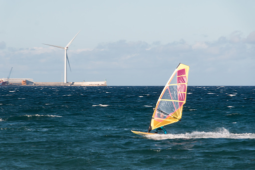 A windsurfer is sailing in Pozo Izquierdo, town of Gran Canaria island with a wind turbine in the background. Water sport concept