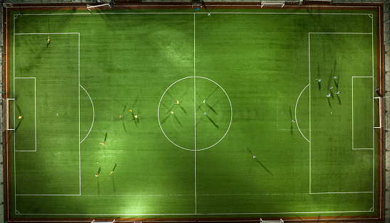 Aerial view of Green football pitch with unrecognizable little player silhouettes; outdoors.