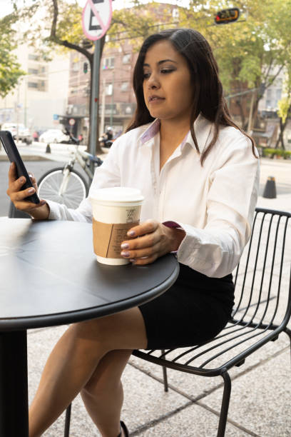 istock Mexican executive woman checking a message on her cell phone while having a coffee at a table in the stree 1400158861