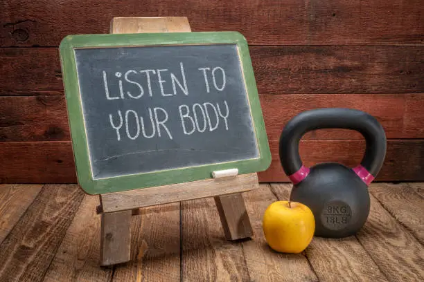 Listen to your body reminder -  slate blackboard sign against weathered red painted barn wood with a kettlebell, wellbeing and fitness concept