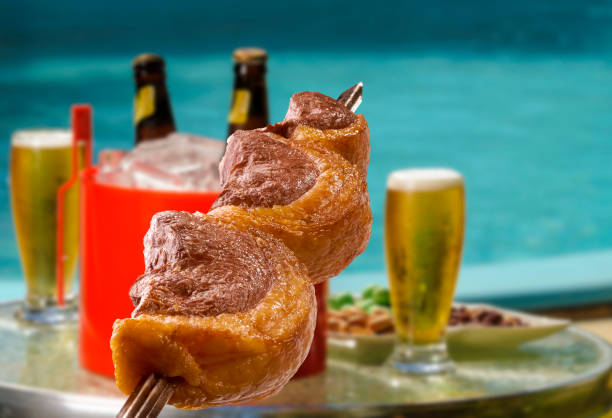Brazilian barbecue picanha on skewers with blurred beers and pool in the background. stock photo