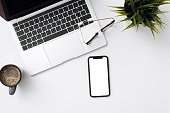 Flat lay photo of office table with laptop, smartphone mockup, house plant and glasses on white copy space background
