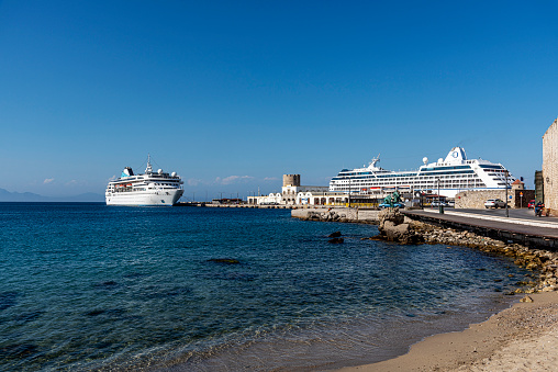 Rhodes, Greece - May 23, 2022: Huge luxury cruise ships bring tourists all summer long in the new Mandraki port of the City of Rhodes, in the Dodecanese islands, Greece, surrounded by fortress stone walls.