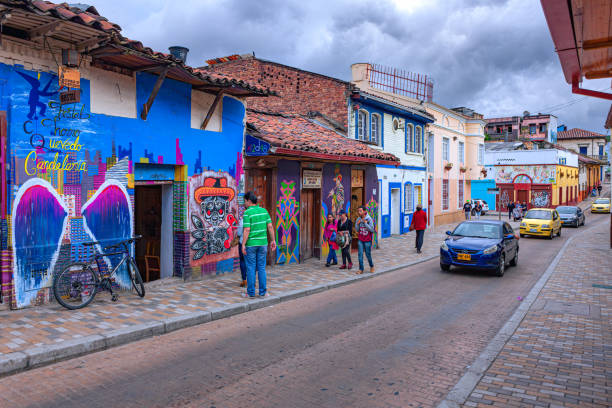bogotá, colombia - los autos conducen y la gente camina por las coloridas calles del histórico distrito de la candelaria en la capital sudamericana. - graffiti paintings men walking fotografías e imágenes de stock