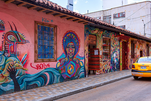 Bogota, Colombia - May 28, 2018: A colorful street in the historic La Candelaria District in the capital city of Bogota in the South American country of Colombia. Many of the walls in the area are painted in the vibrant colours of Colombia, sometimes depicting Pre-Colombian legends or modern Street Art and Graffiti. The altitude at street level is 8,660 feet above mean sea level. Photo shot in the late afternoon sunlight; horizontal format.