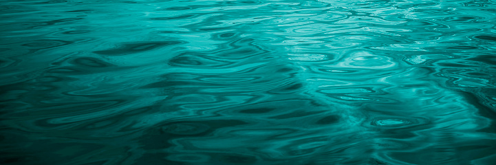 Blue-green water background. Reflection of light on the wavy surface of the water. Ripples. Beautiful teal background with copy space for design. Web banner. Wide. Panoramic.