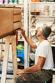 istock Senior male carpenter polishing the edge of old wood chest cabinet 1400174819