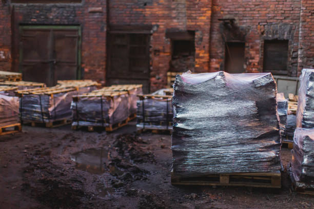 Red bricks are stacked in neat rows at a construction site, bathed in warm afternoon sunlight with greenery in the background.