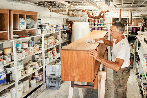 Senior male carpenter cleaning wooden chest drawer with a cloth after renovation in his workshop