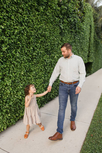 31-year-old american father walking down a sidewalk with his 3-year-old daughter while holding hands in palm beach, florida in the spring of 2022 - hedge multi ethnic group people holding hands imagens e fotografias de stock