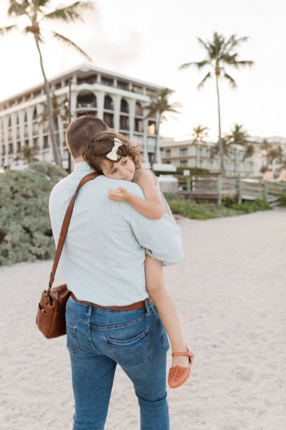 31-year-old american father walking while holding his 3-year-old daughter while having her head on his shoulder in palm beach, florida in the spring of 2022 - hedge multi ethnic group people holding hands imagens e fotografias de stock