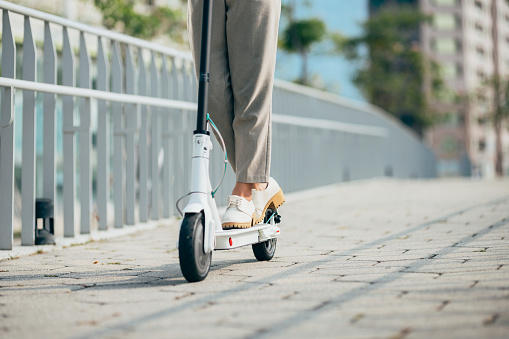 Asian businesswoman riding an electric scooter to commute to works place. Green incentive promoting the usage of electric scooters.