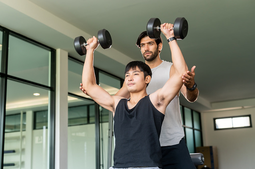 Man exercise in gym with trainer to assistFitness trainer assisting customer for working out during exercise