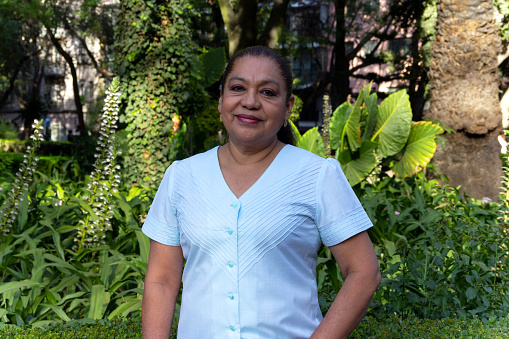 Mature Mexican woman looking at the camera smiling, standing, background of trees and green foliage. Latin woman looking at camera smiling. cheerful attitude