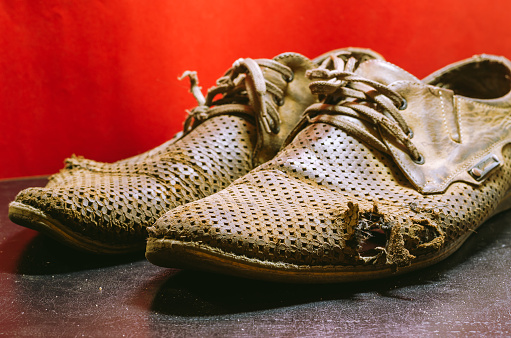 Close view of a pair of used rustic safety shoes on a white wooden floor. Taken indoors with natural light coming from  a window