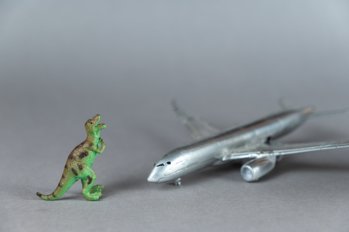 Children's toys. Silver airplane and dinosaur miniature against a gray background. Small green figure of a predatory dinosaur standing on its hind legs. Toy airplane. Selective focus.