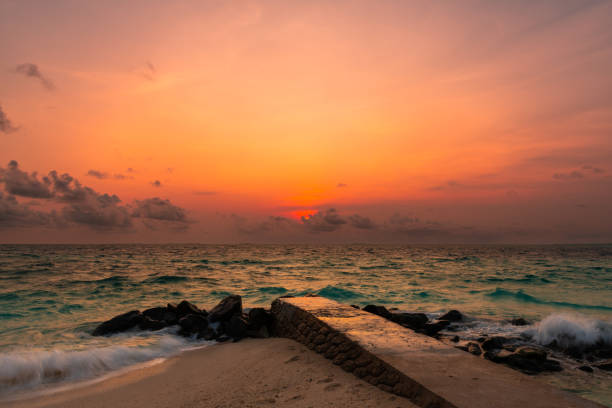 View of a beautiful sunset from the beach with a pier in the foreground leading into the turquoise waters of the ocean in the Maldives.