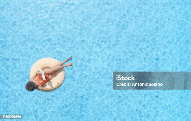 Anonymous Ethnic Lady Floating On Rubber Ring In Swimming Pool And Reading Book Stock Photo - Download Image Now