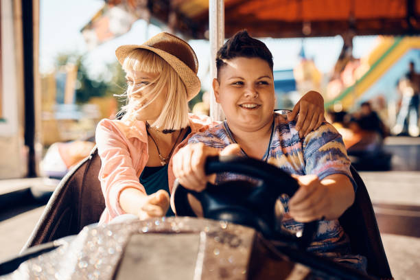 istock Young lesbian and her girlfriend driving bumper car at amusement park. 1400200438