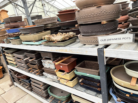 Stock photo showing close-up view of stack of ceramic glazed clay bonsai pots, piled in rows on metal shelves at a garden centre.