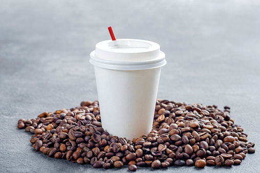 Close up view of a white plastic cup and coffee beans with textured background