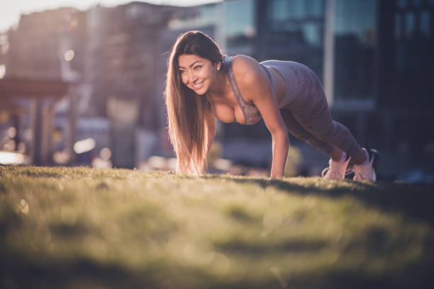 Young smiling woman exercising in public park while doing push ups