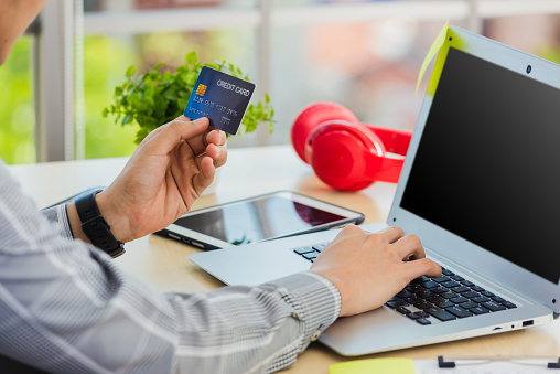 Asian business man hand holding credit card and typing entering security code on a laptop computer for process payment online shopping on the internet at the home office