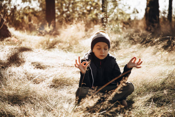 A child in warm clothes meditates in the forest while sitting on the grass while walking. Portrait of a boy