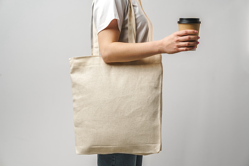 Cropped woman with cotton bag and paper coffee cup, studio shot, close up