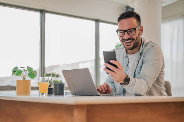 istock Cheerful businessman messaging on smart phone while working on laptop at office desk 1400209965