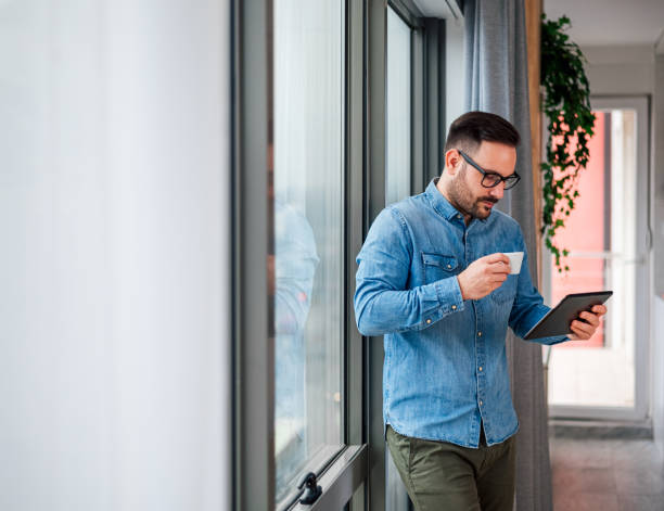 istock Young businessman using digital tablet while enjoying coffee by window at office 1400210001