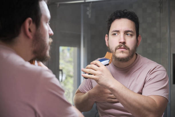 riflesso del giovane che si rade con il trimmer davanti allo specchio. - shaving men electric razor reflection foto e immagini stock