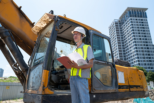 Male engineer working next to construction machinery at construction site