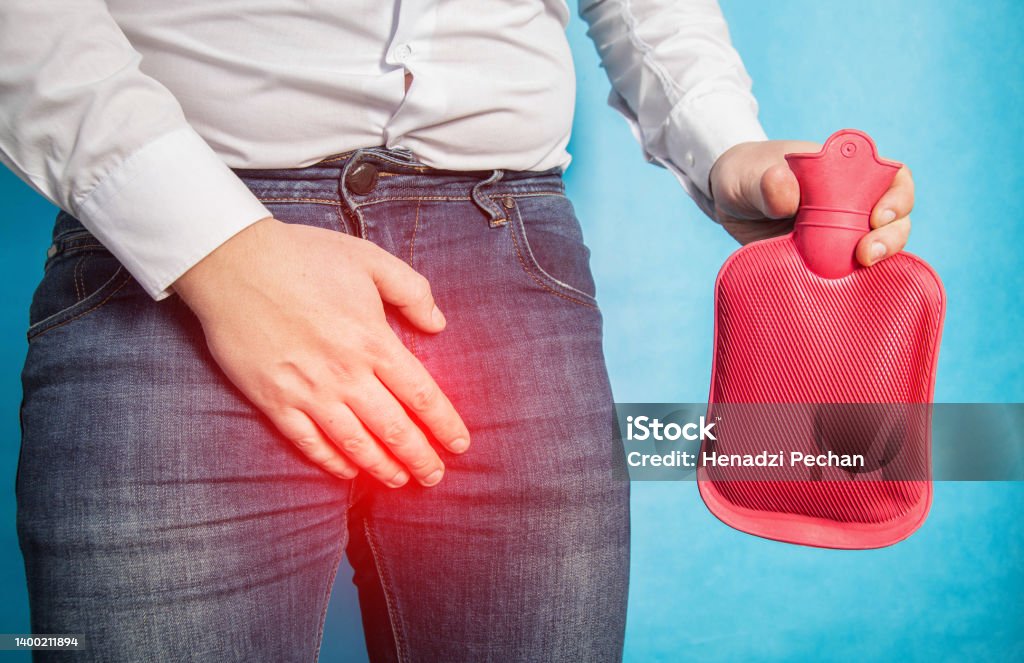 A man in a white shirt holds his groin and holds a red heating pad with hot water in his hand. The concept of treatment of male diseases in the genital area. Close-up A man in a white shirt holds his groin and holds a red heating pad with hot water in his hand. The concept of treatment of male diseases in the genital area. Testis Stock Photo A man in a white shirt holds his groin and holds a red heating pad with hot water in his hand. The concept of treatment of male diseases in the genital area. Close-up A man in a white shirt holds his groin and holds a red heating pad with hot water in his hand. The concept of treatment of male diseases in the genital area. Testis Stock Photo