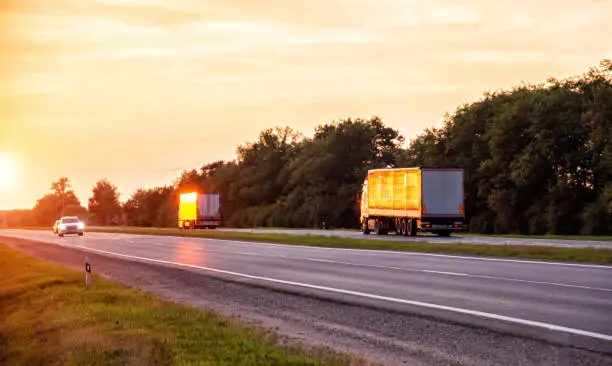 Photo of a convoy of trucks delivers cargo along the highway in the evening at sunset. The concept of cargo transportation and logistics companies FTL