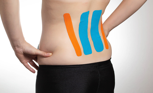 Kinesiological tape orange and blue on the back of the lumbar spine of the girl. Taping problem areas and pain relief, close-up